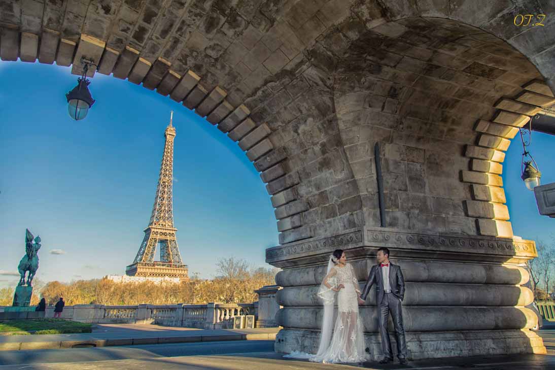 Wedding couple beneath a stone arch with the Eiffel Tower beyond
